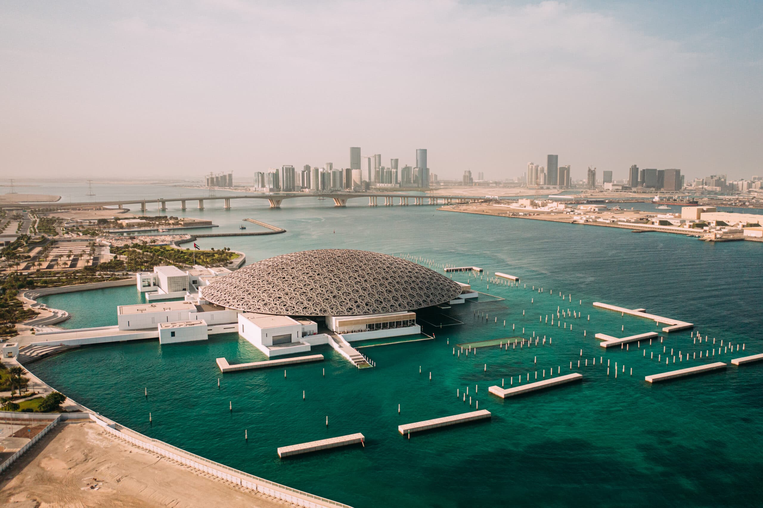 The Louvre Abu Dhabi dome on the water from the air, the towers of Al Reem on the horizon