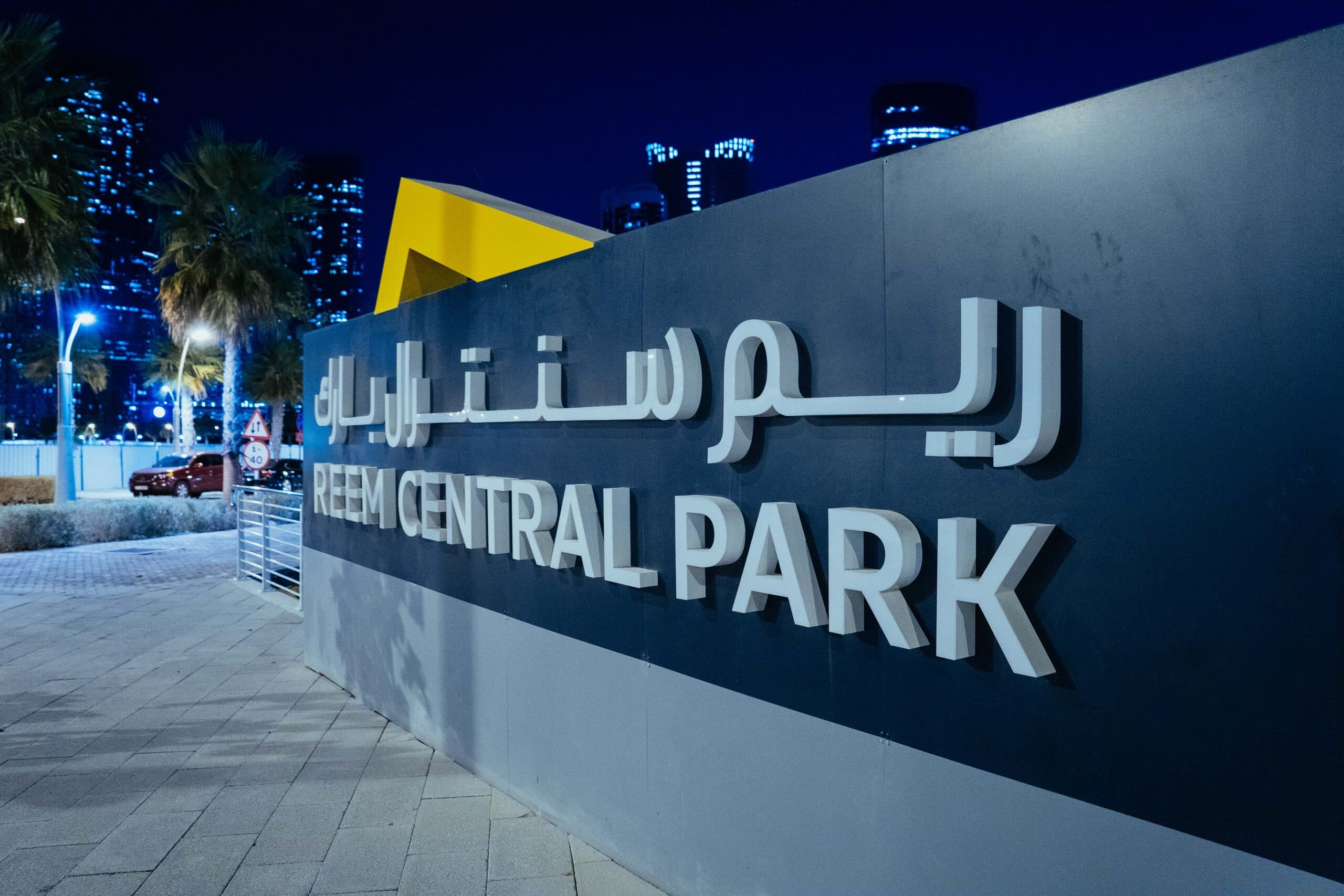 The Reem Central Park sign at night, the island's towers lit behind it