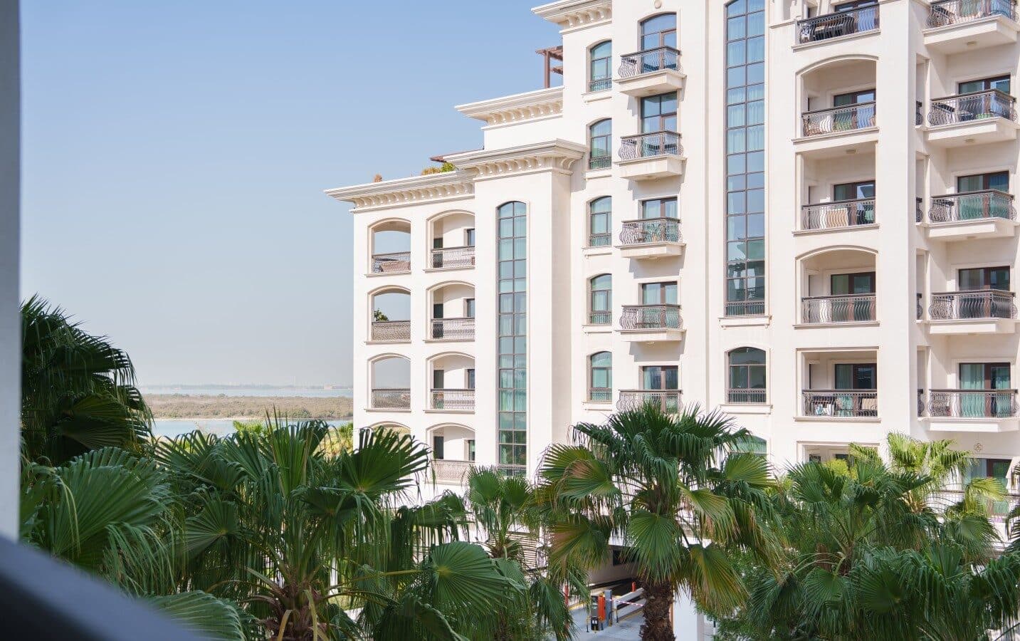An Ansam building's arched white facade above the palm garden