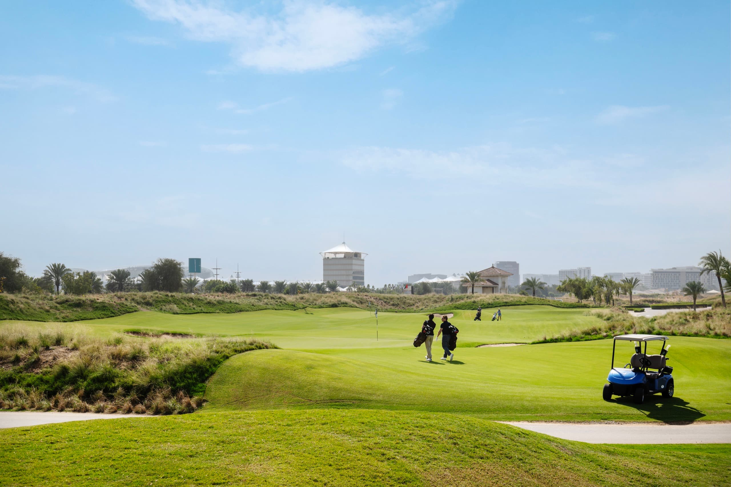 A fairway at Yas Links with golfers and a buggy in the distance